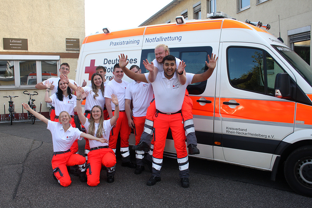 Gruppe mit 10 neuen Auszubildenden jubelt vor einem Krankenwagen