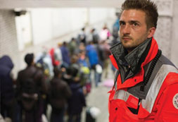 Rettungssanitäter, im Hintergrund Flüchtlinge 