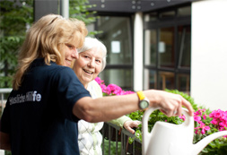 Junge Frau hilft einer Seniorin beim Blumen gießen
