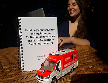 Rebekka an einem Laptop, vor ihr ein Heft mit Handlungsempfehlungen für Notfallsanitäter