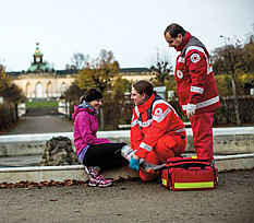 Junge Frau sitzt auf dem Boden und wird von zwei Helfern vor Ort betreut