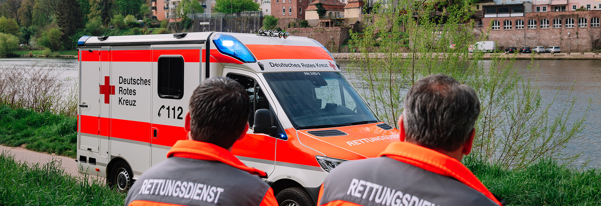 Zwei Notfallsanitäter mit einem Rettungswagen am Ufer des Neckars