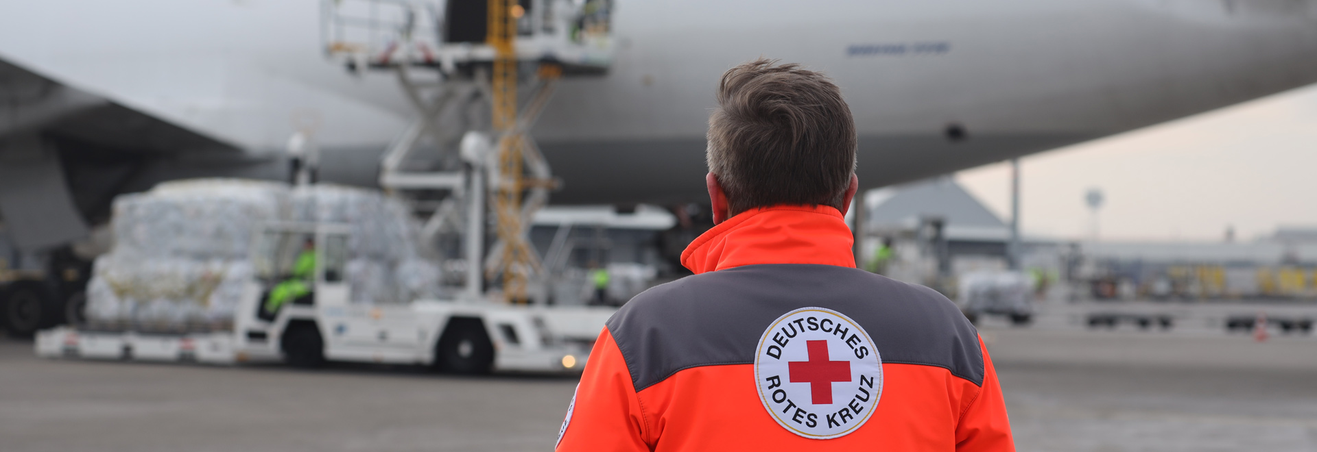 DRK-Mitarbeiter blickt auf ein Flugzeug, das mit Hilfsgütern beladen wird.