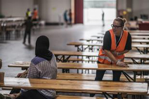 Helferin wischt einen Tisch ab und unterhält sich mit einem Flüchtling