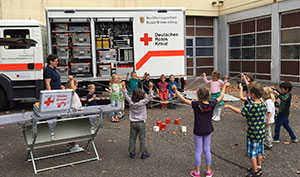 Kinder versuchen gemeinschaftlich mit Seilen das Rote Kreuz aus Holzklötzen zu bauen