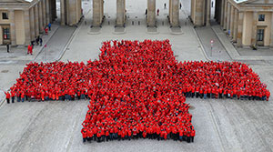 Menschen mit Roten Jacken bilden vor dem Brandenburger Tor ein rotes Kreuz
