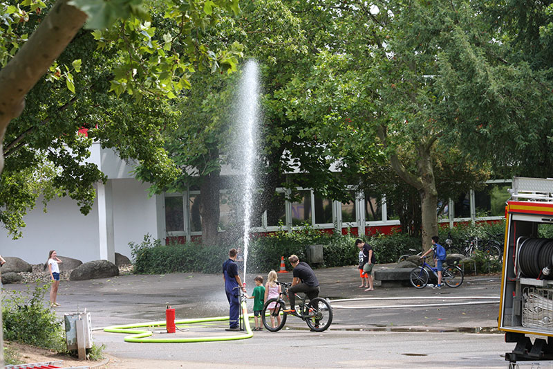Ein Feuerwehrmann spritzt mit einem Schlauch Wasser in den Schulhof