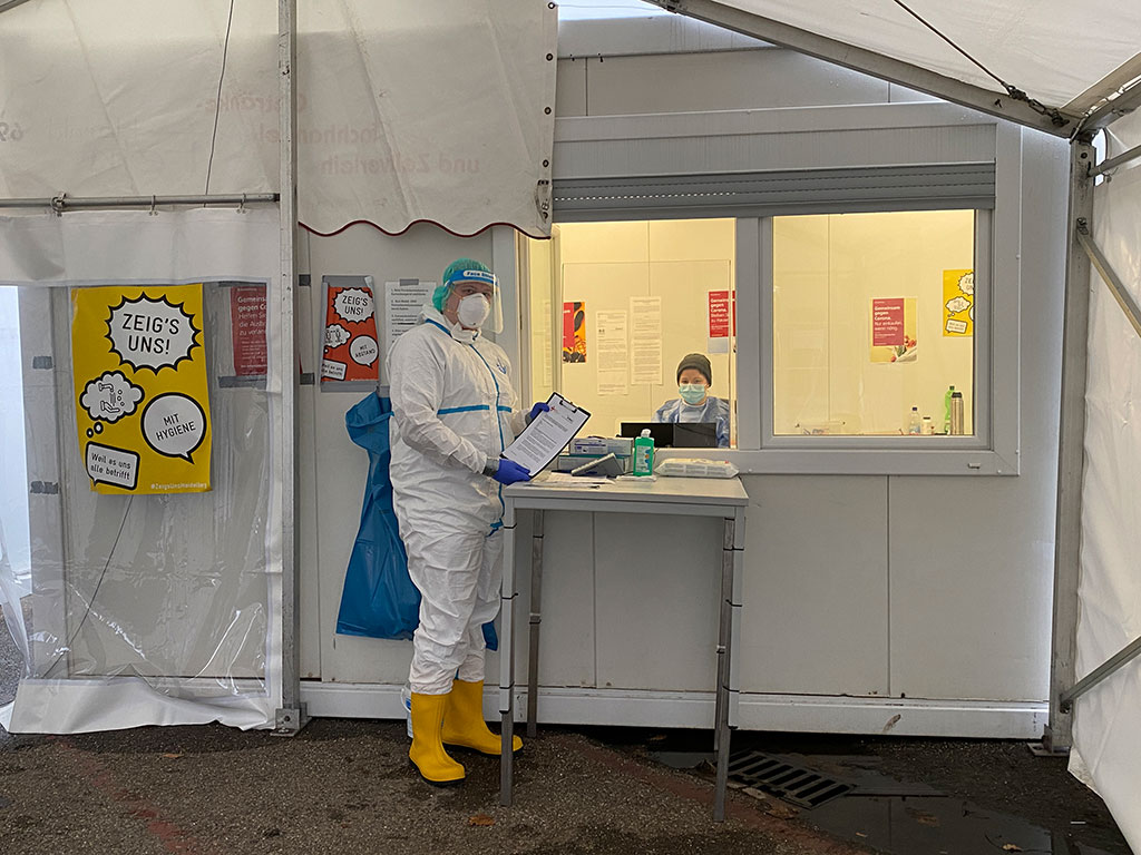 DRK-Mitarbeiter mit Schutzkleidung zeigt einen Fragebogen