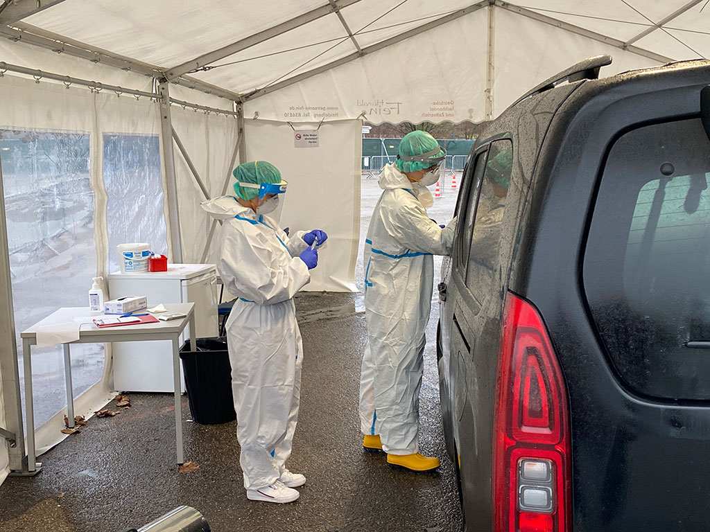 Zwei DRK-Mitarbeiter an einem Auto beim Corona-Test