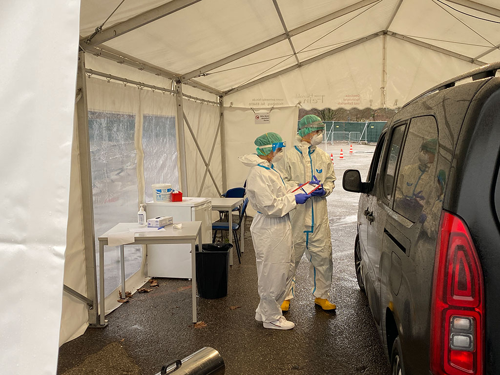 DRK-Mitarbeiter mit Schutzkleidung notiert etwas bei einen Corona Schnelltest in der Drive-In Teststation auf einem Formular