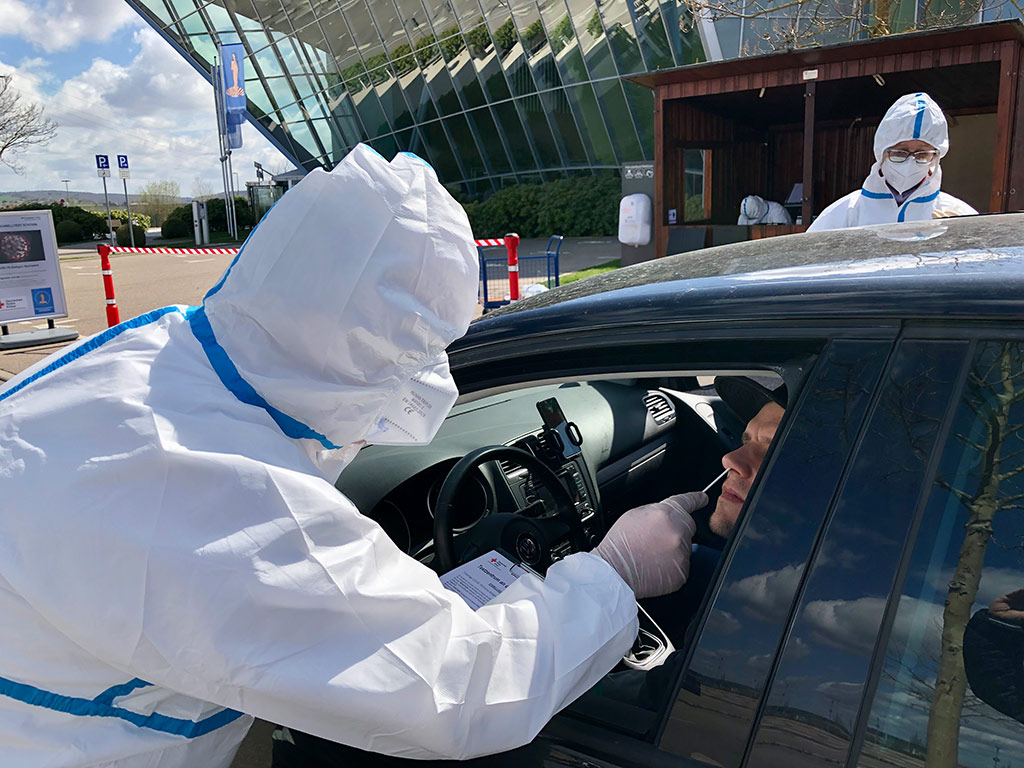 DRK-Mitarbeiter in Schutzkleidung macht im Drive-In einen Schnelltest