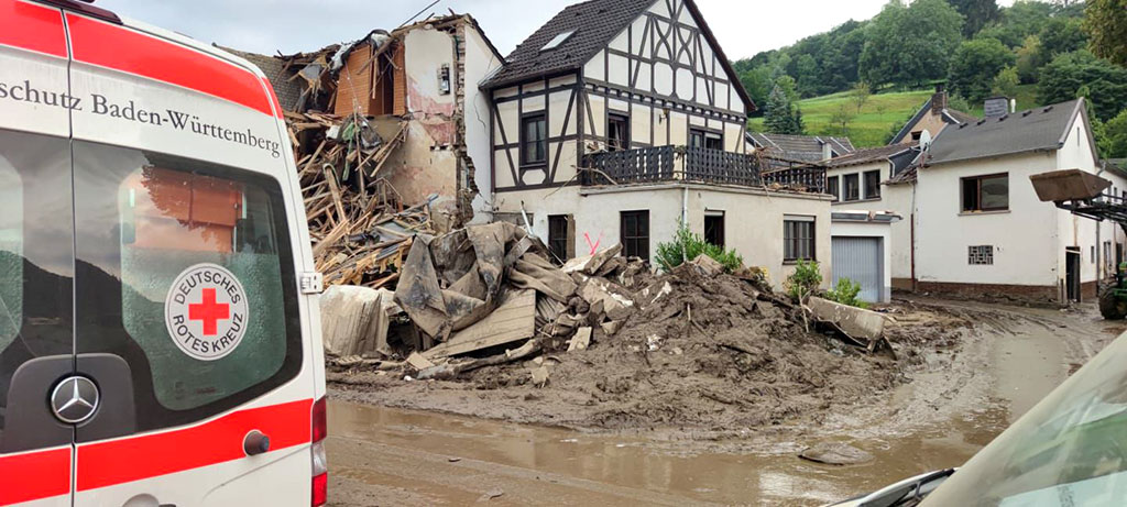 DRK-Fahrzeug neben Schlamm- und Schuttmassen bei Wohnhäusern