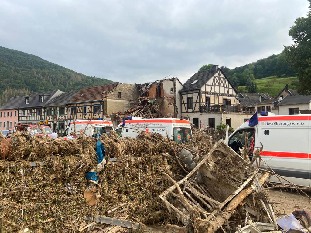 Hintereinander geparkte DRK-Fahrzeuge neben Dreck und Schutt des Hochwassergebietes