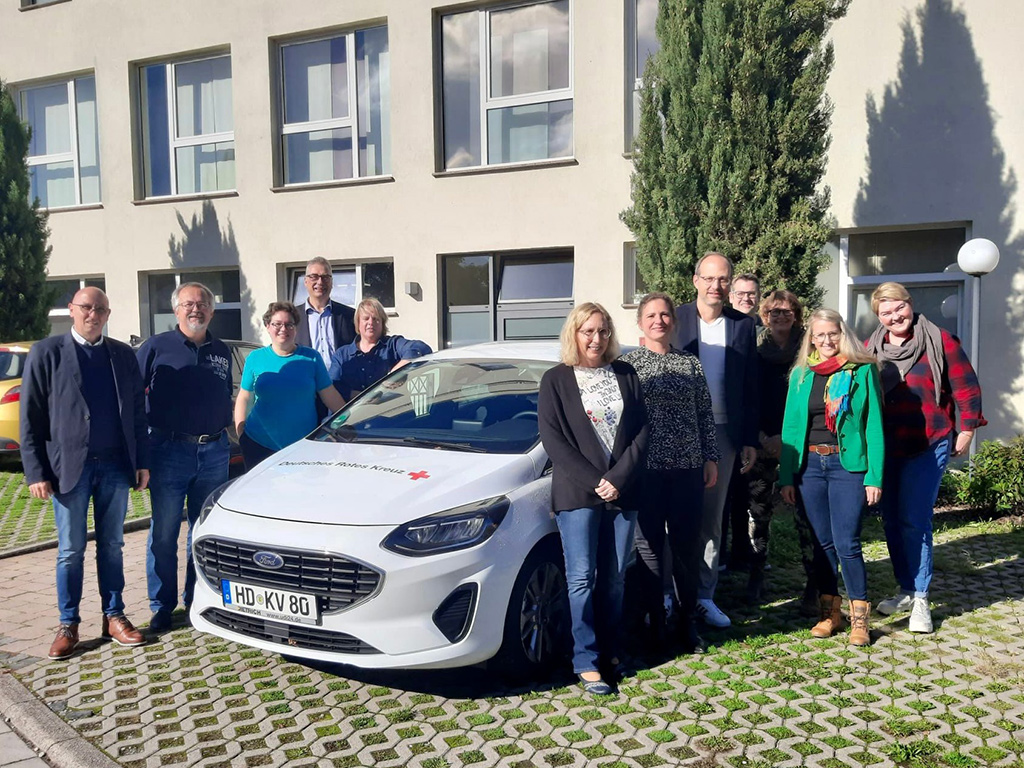 Bild größer ansehen Mitglieder des Präsidiums neben einem Fahrzeug des DRK vor einem Gebäude