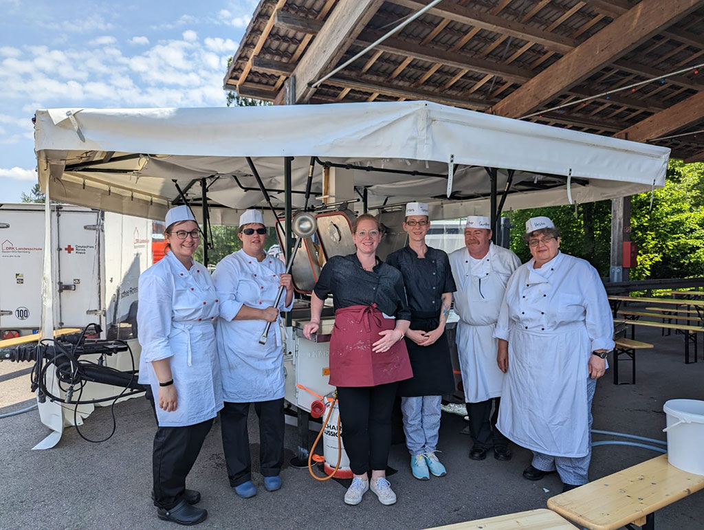 Sechs neu Feldköche vor einer offenen Küche im Freien