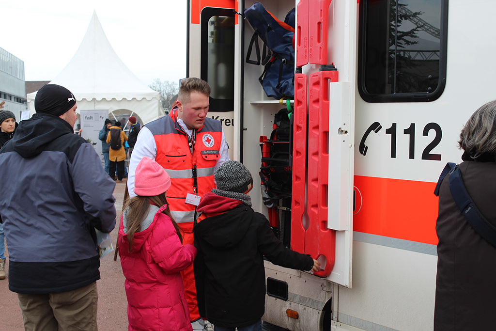 Ein DRK-Mitarbeiter erklärt zwei Kindern den Rettungswagen