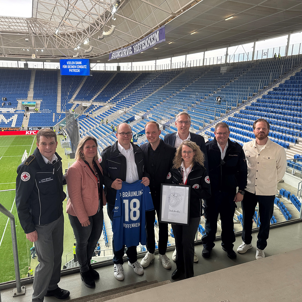 Gruppenbild von der Verabschiedung von Patrick Bräunling (im Bild mit einem TSG-Trikot mit der Nimmer 18) mit Vertreter*innen des DRK Kreisverbandes Rhein-Neckar/Heidelberg und der TSG Hoffenheim.
