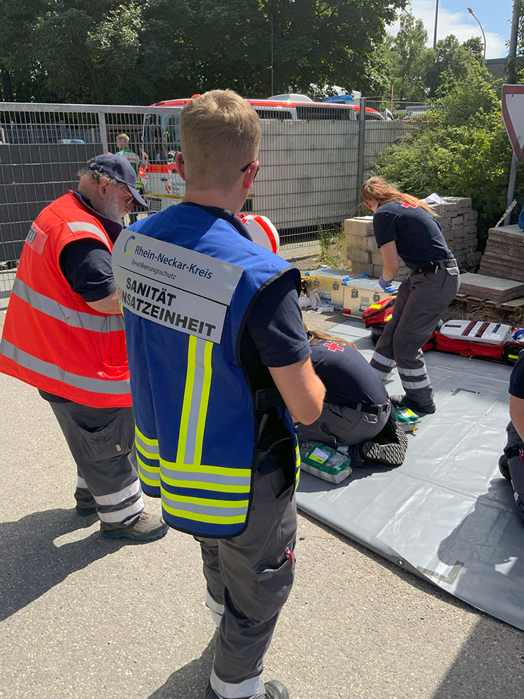 Ein Mitarbeiter der Sanität Einsatzeinheit steht vor Sanitätern, die sich um eine verletzte Person kümmern