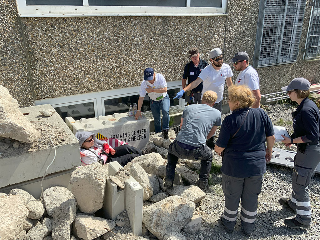 Helfer bei einer verletzten Person neben Schutthaufen