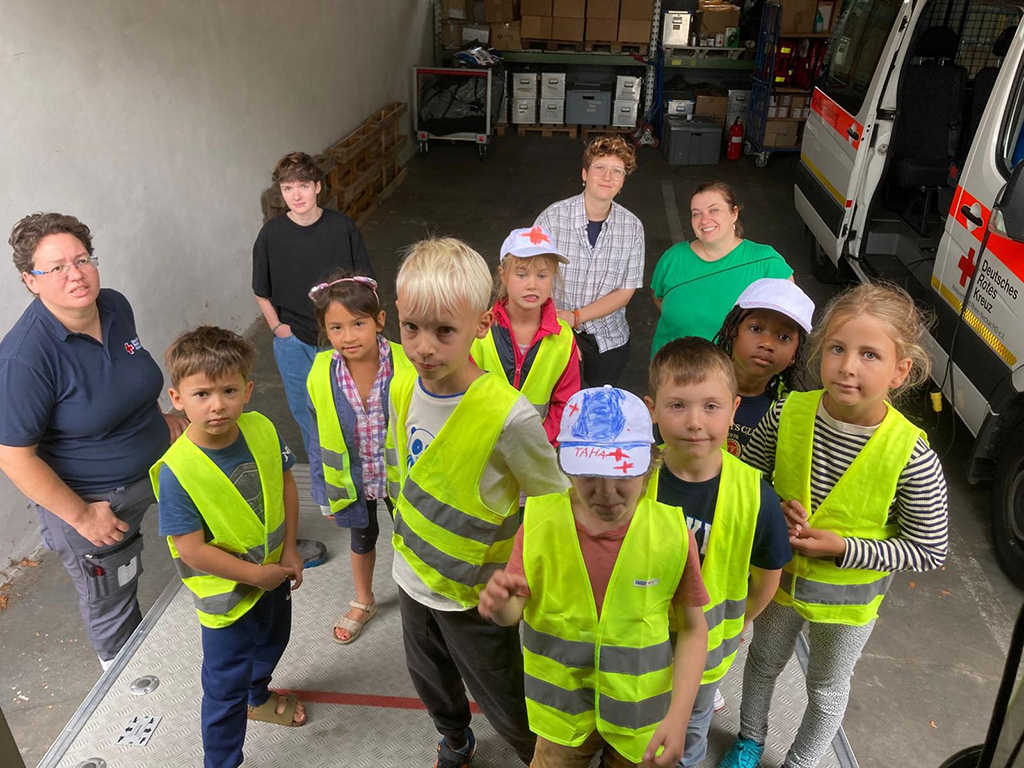 Gruppenbild mit Betreuerinnen und 8 Kindern neben einem Rettungswagen