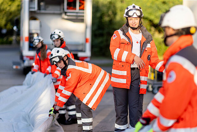 DRK-Mitarbeiter des Katastrophenschutzes breiten auf dem Boden eine weiße Plane aus