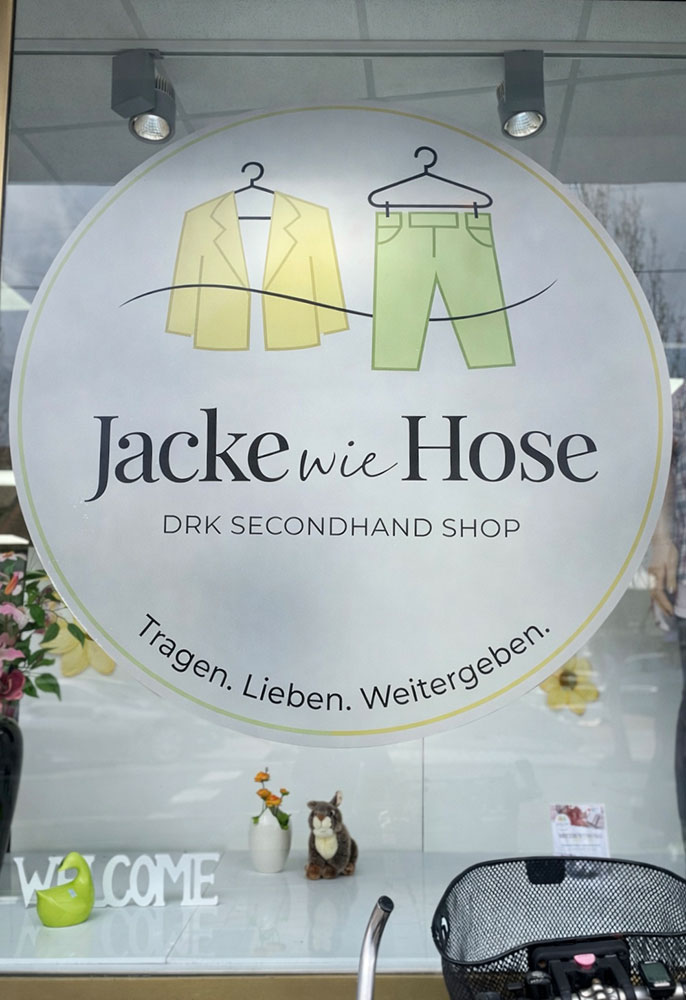 Das große, runde Logo von Jacke wie Hose an der Schaufensterscheibe