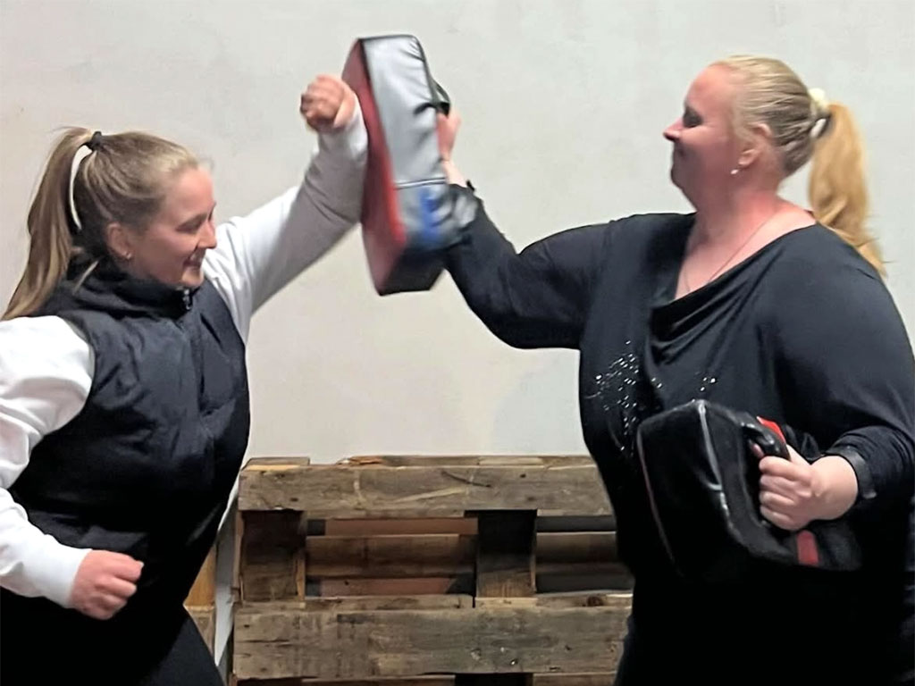 Zwei Frauen üben Selbstverteidigung: eine Frau wehrt mit dem Unterarm einen Angriff einer anderen Frau ab