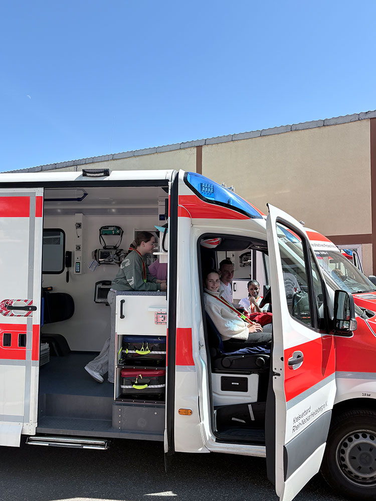 Zwei Mädchen sitzen vorne in einem Rettungswagen, ein Mädchen erkundet den hinteren Teil des RTW