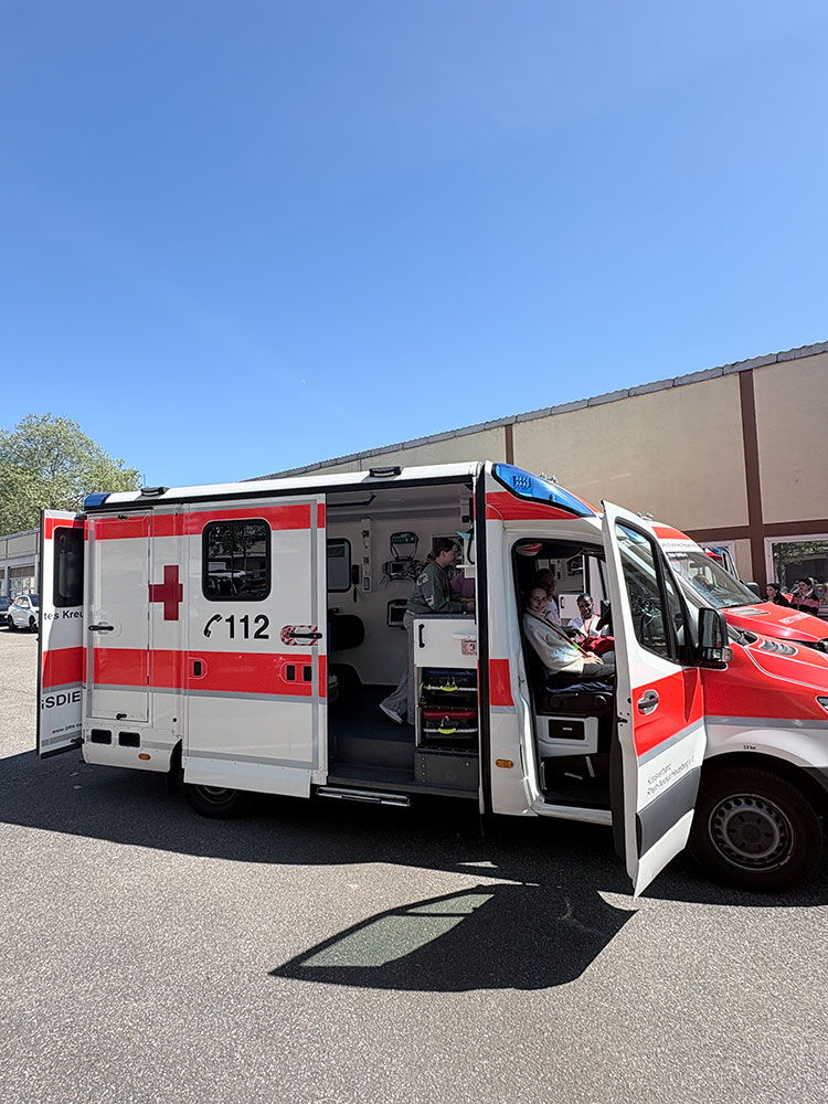 Zwei Mädchen sitzen vorne in einem Rettungswagen, ein Mädchen erkundet den hinteren Teil des RTW