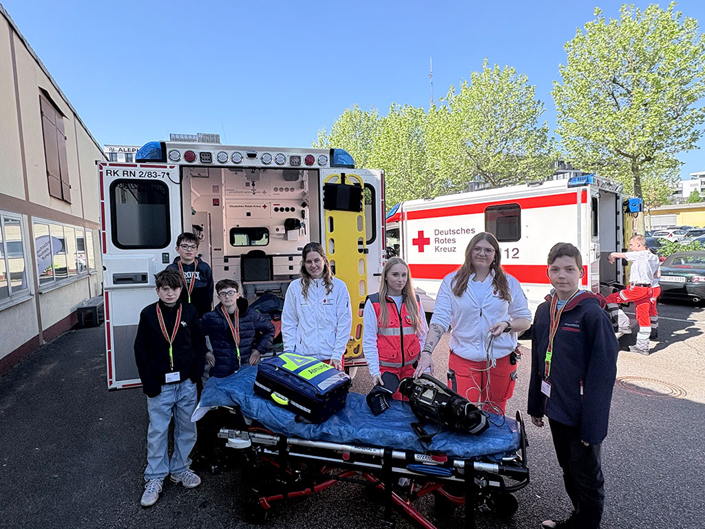 Drei DRK-Mitarbeiterinnen zeigen vier Jungs verschiedene Bestandteile eines Rettungswagens