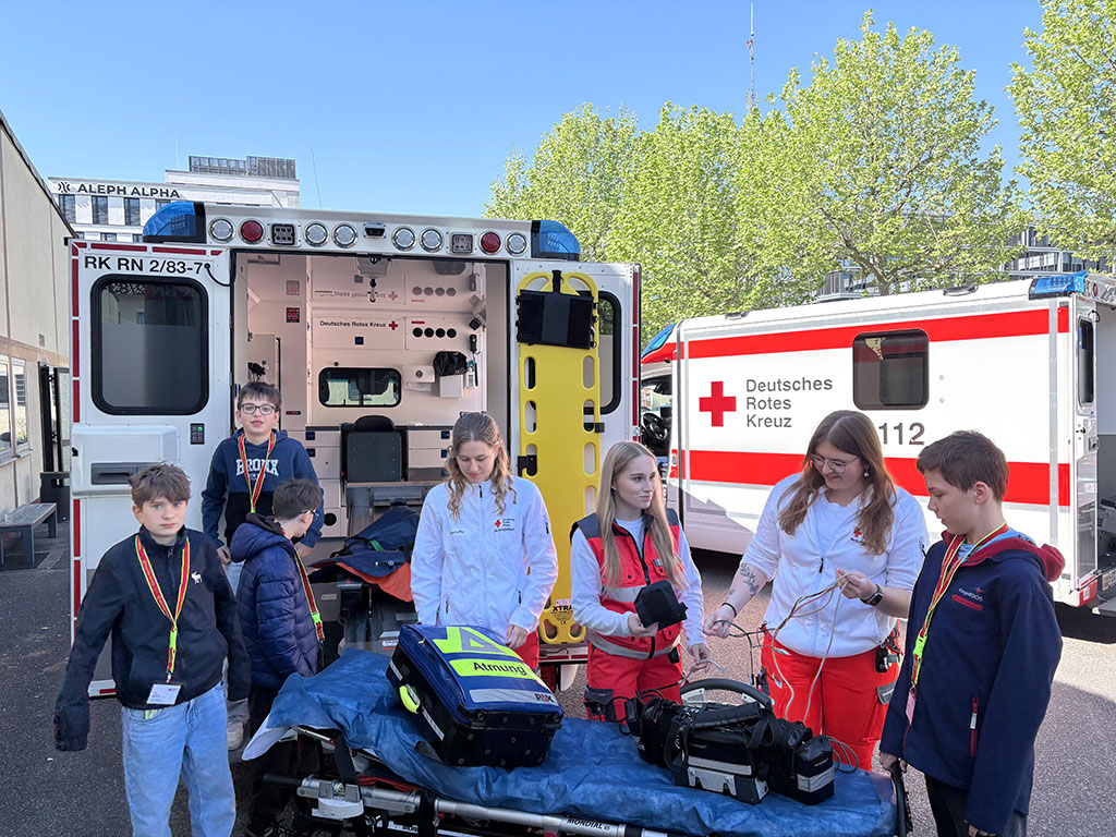 Drei DRK-Mitarbeiterinnen zeigen vier Jungs verschiedene Bestandteile eines Rettungswagens