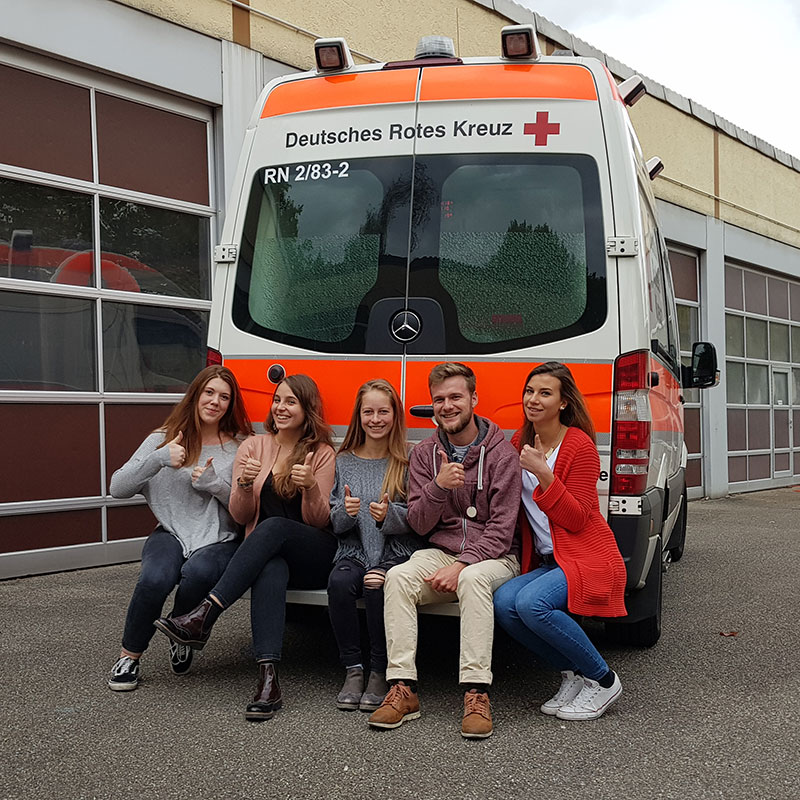Fünf Auszubildende vor dem Heck eines Krankenwagens
