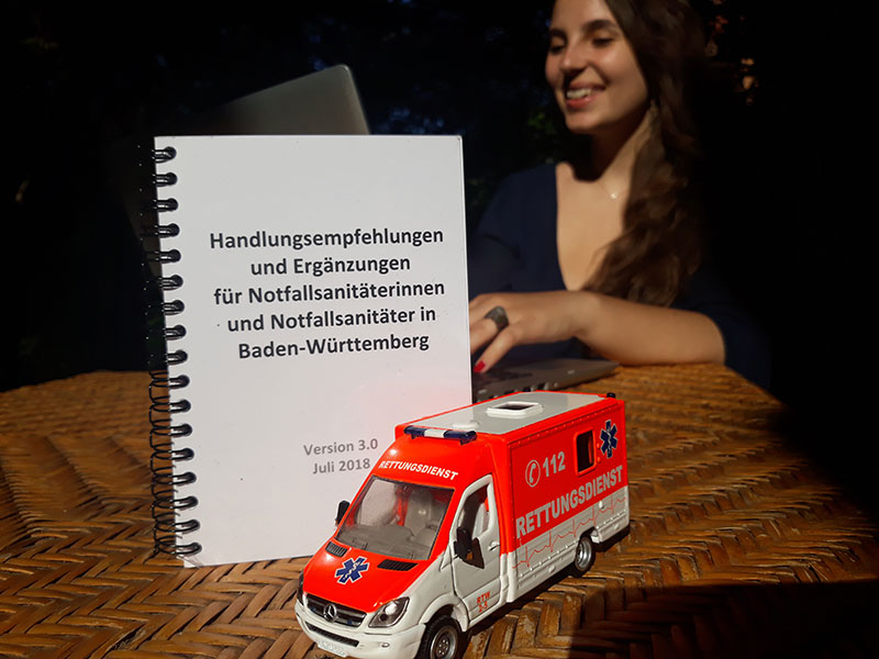 Rebekka an einem Laptop, vor ihr ein Heft mit Handlungsempfehlungen für Notfallsanitäter