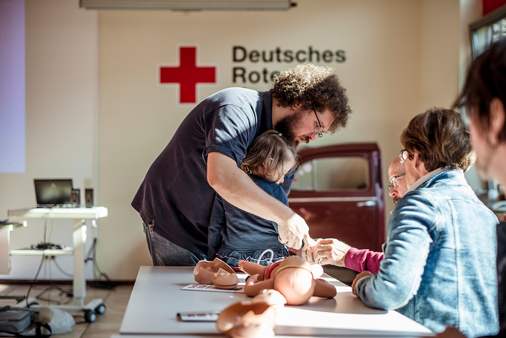 Eltern beobachten beim Kurs Erste Hilfe am Kind die Behandlung der Hand eines Mädchens; Foto: Thilo Ross