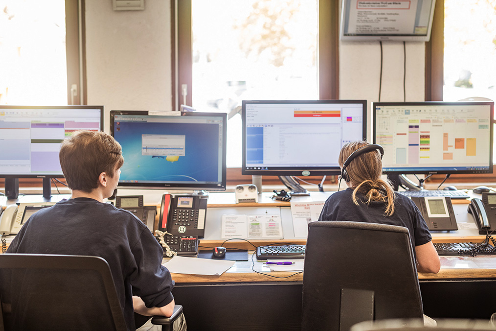 Zwei Mitarbeiter sitzen vor mehreren Computer-Bildschirmen
