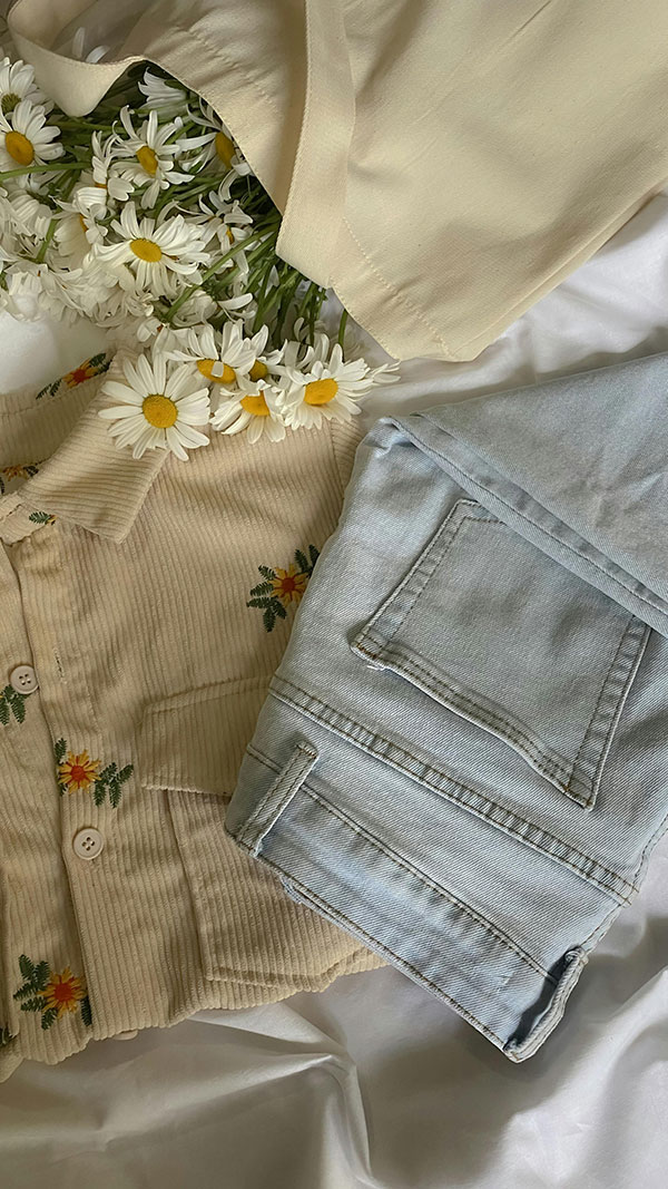Hellblaue Jeans und eine beige Bluse mit Blumen liegen auf einem Tisch
