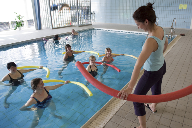 Fünf Frauen im Wasser eines Schwimmbades, Trainerin am Beckenrand