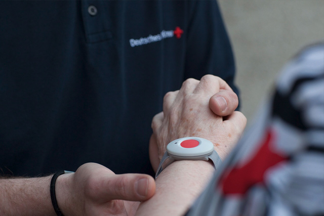 Informationen zum Hausnotruf Hausnotrufknopf am Handgelenk einer älteren Dame