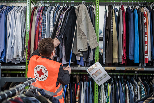 Zu den Informationen zum Kleiderladen DRK-Mitarbeiterin hängt Kleidung ins Regal