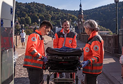 Drei DRK-Mitarbeiter bereiten einen Krankentransport vor